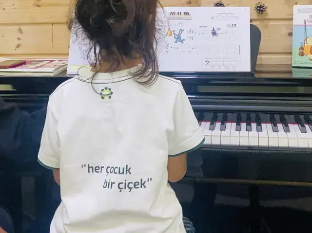 Piyano başında nota defterine bakan bir çocuk, arkadan